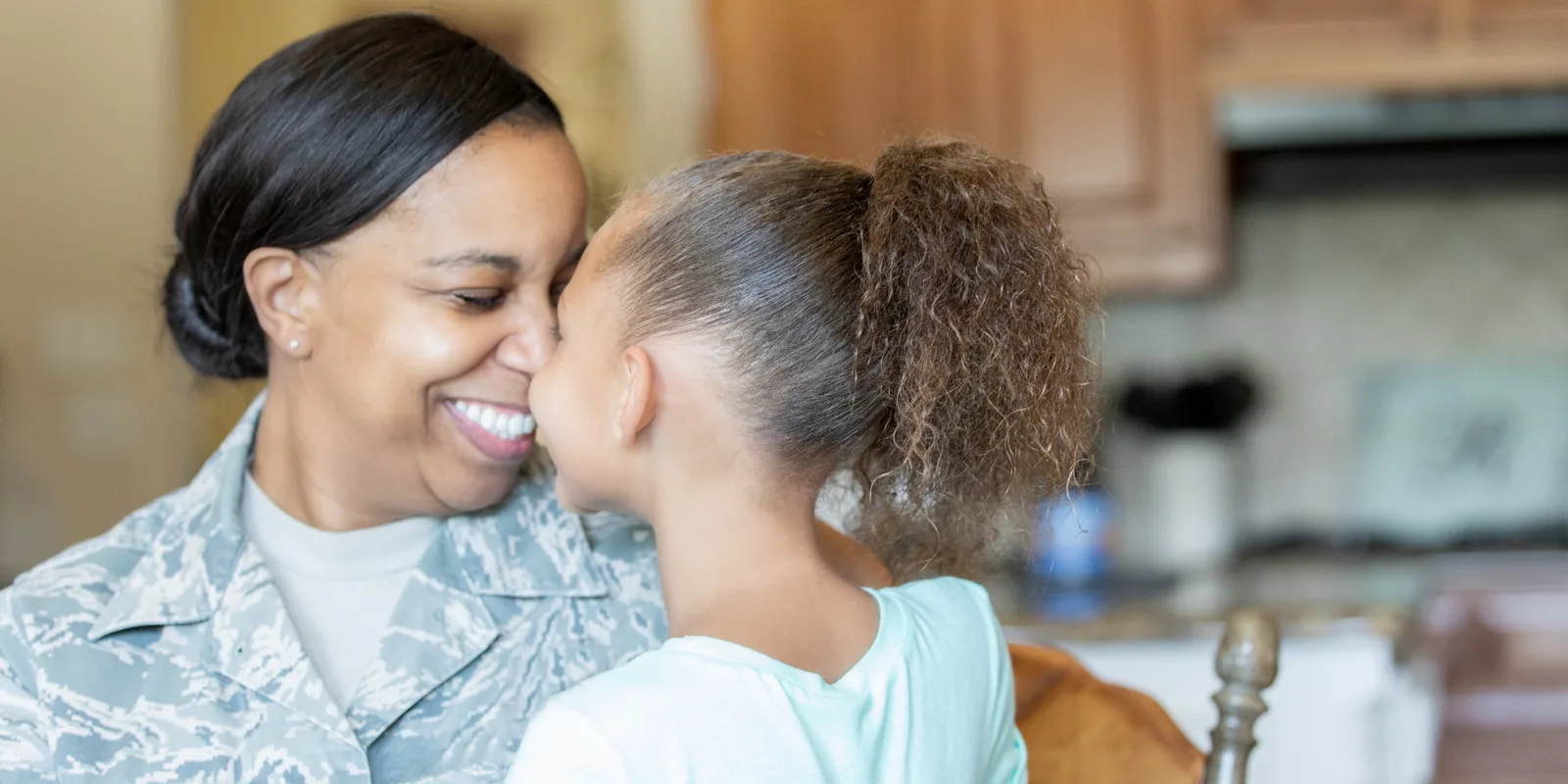 A smiling service member sharing a warm moment with her daughter at home